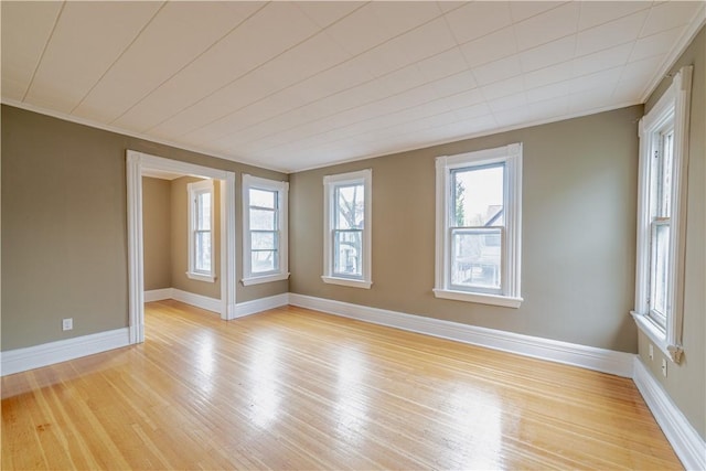 empty room with light wood-style floors, baseboards, and crown molding