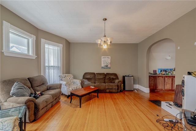 living area with light wood-style floors, arched walkways, and an inviting chandelier