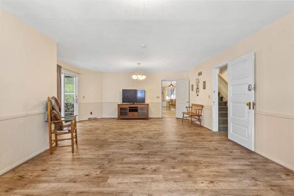 living room featuring a wainscoted wall, stairs, wood finished floors, and a notable chandelier