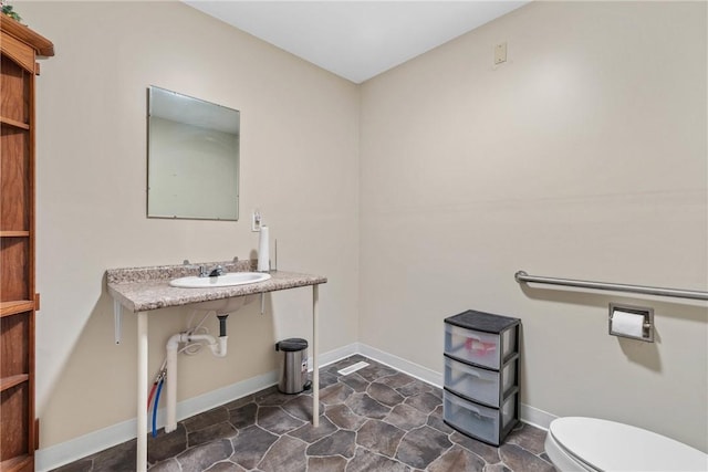 bathroom with toilet, baseboards, stone finish flooring, and a sink