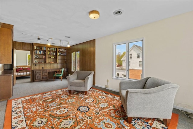 living area with carpet floors, wood walls, baseboards, and visible vents