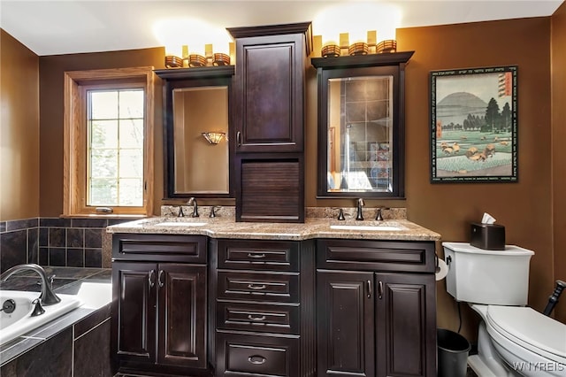 full bathroom featuring double vanity, tiled bath, toilet, and a sink