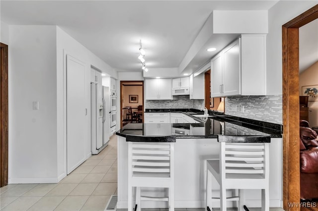 kitchen featuring white cabinets, white appliances, a peninsula, light tile patterned floors, and backsplash
