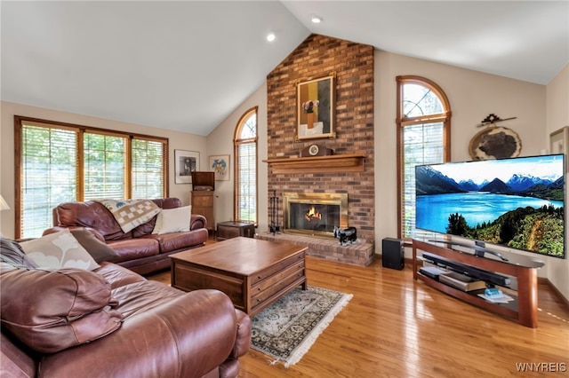 living area with high vaulted ceiling, plenty of natural light, a fireplace, and wood finished floors
