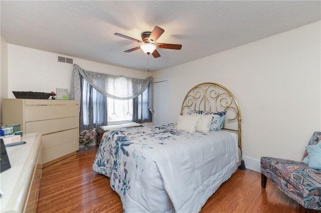 bedroom featuring a ceiling fan, a textured ceiling, visible vents, wood finished floors, and baseboards