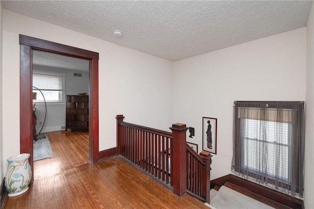 hall with baseboards, a textured ceiling, wood finished floors, and an upstairs landing