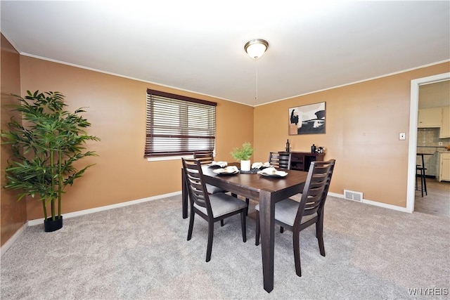 dining room featuring visible vents, baseboards, crown molding, and light colored carpet