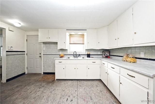 kitchen with a sink, white cabinetry, a wainscoted wall, and light countertops