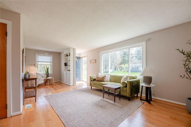 living room featuring visible vents, a textured ceiling, light wood finished floors, and baseboards