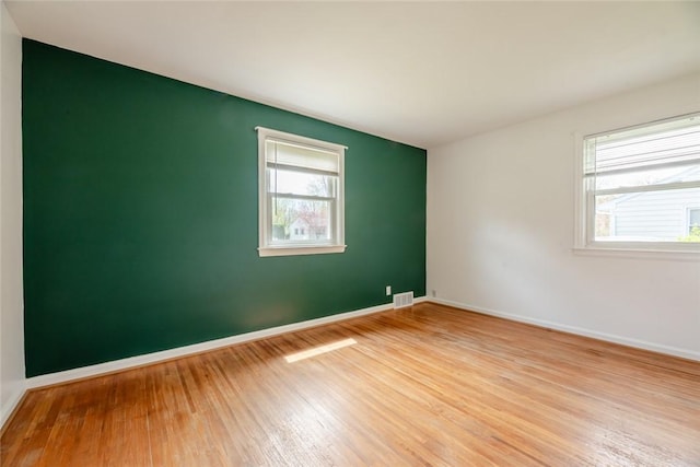 empty room featuring a healthy amount of sunlight, baseboards, wood finished floors, and visible vents