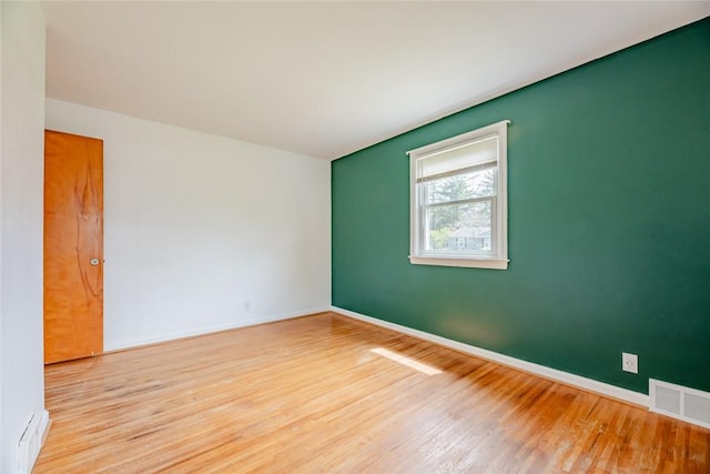 spare room with baseboards, visible vents, and wood finished floors