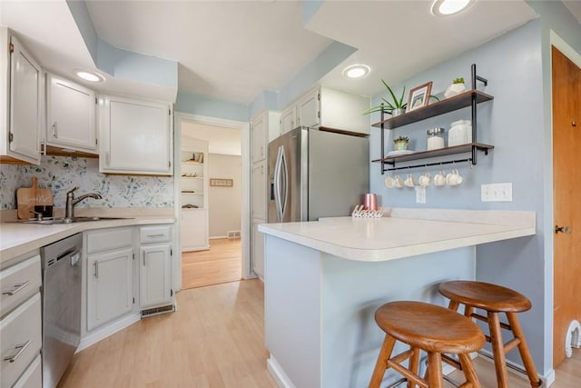kitchen featuring a peninsula, a kitchen bar, light wood-type flooring, a sink, and stainless steel appliances