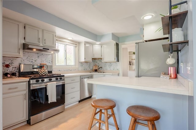 kitchen featuring appliances with stainless steel finishes, a breakfast bar area, a peninsula, backsplash, and under cabinet range hood