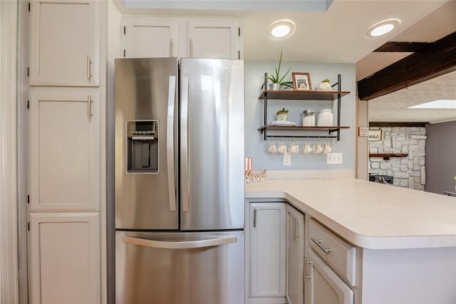 kitchen with a stone fireplace, light countertops, stainless steel fridge with ice dispenser, white cabinets, and a peninsula