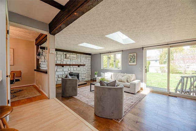 living area featuring a textured ceiling, a stone fireplace, a skylight, visible vents, and wood finished floors