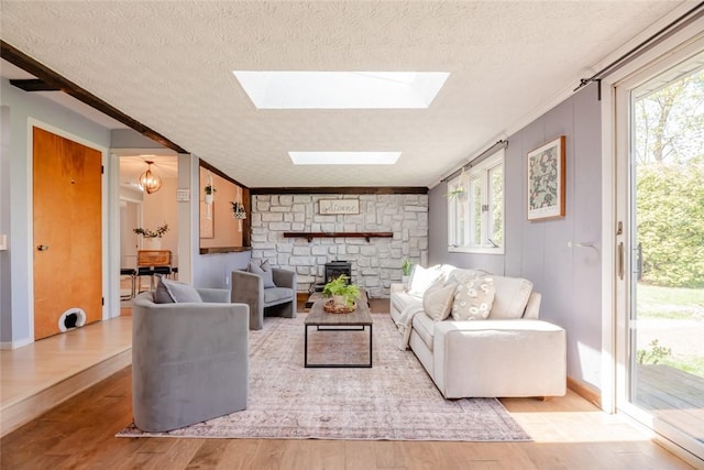living area featuring a stone fireplace, a textured ceiling, wood finished floors, and a skylight