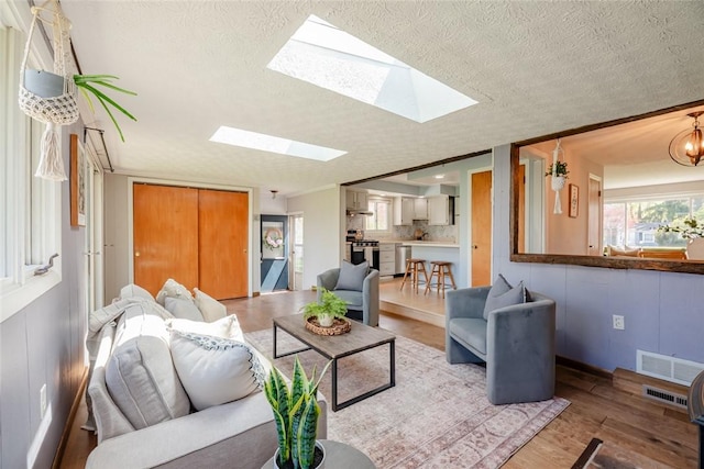 living room featuring visible vents, a textured ceiling, wood finished floors, and a skylight