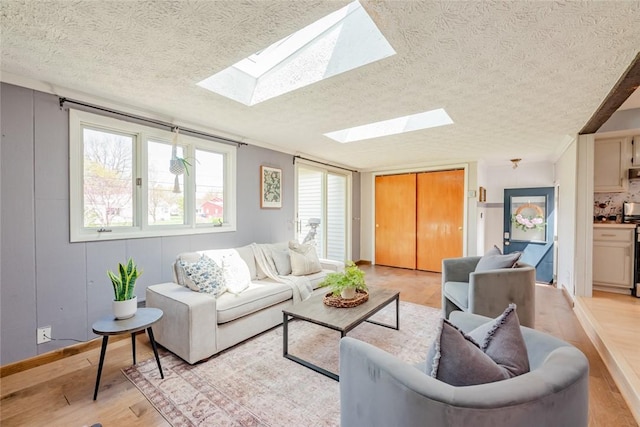 living room with a skylight, baseboards, light wood-style floors, and a textured ceiling
