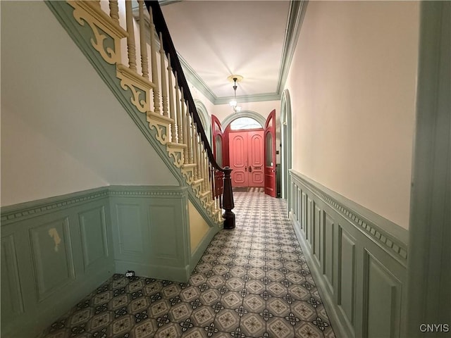 hallway featuring crown molding, wainscoting, stairway, and a decorative wall
