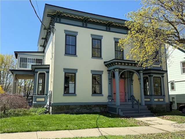 italianate house featuring a porch, stucco siding, and a front lawn