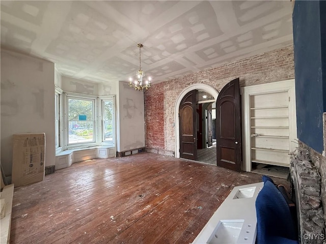 118 E 3rd St, Oswego, NY 13126 - unfurnished living room with brick wall, a chandelier, wood-type flooring, and arched walkways