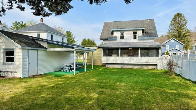 back of property featuring a yard, fence, a shingled roof, and a sunroom
