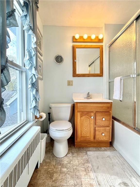 bathroom featuring vanity, combined bath / shower with glass door, radiator heating unit, and toilet