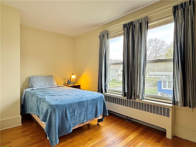 bedroom with radiator heating unit, baseboards, and hardwood / wood-style flooring
