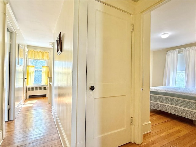 hallway featuring radiator heating unit, baseboards, and light wood-type flooring