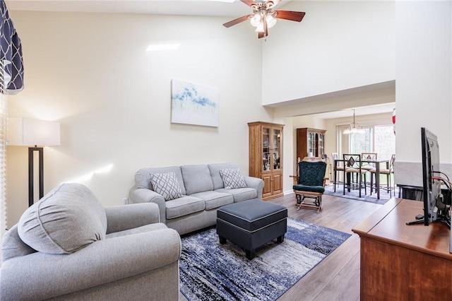 living area featuring ceiling fan with notable chandelier, wood finished floors, and a towering ceiling