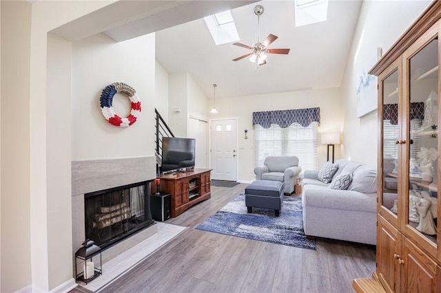 living room with ceiling fan, a fireplace, high vaulted ceiling, wood finished floors, and a skylight