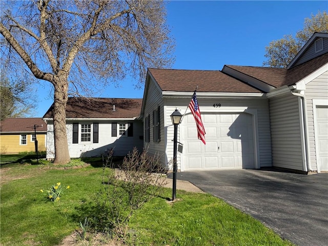 view of front of home featuring roof with shingles, an attached garage, a front yard, and aphalt driveway