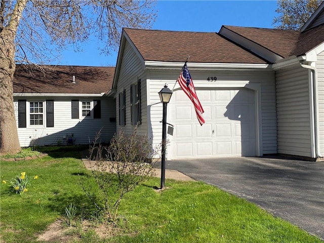 view of side of property featuring a lawn, a garage, driveway, and a shingled roof