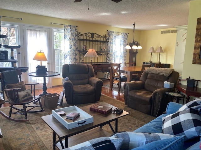 living area with ceiling fan with notable chandelier, a textured ceiling, and visible vents
