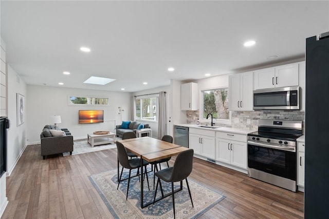 kitchen featuring open floor plan, tasteful backsplash, a sink, a skylight, and stainless steel appliances