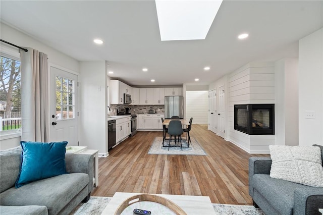 living area with recessed lighting, light wood-style flooring, and a multi sided fireplace