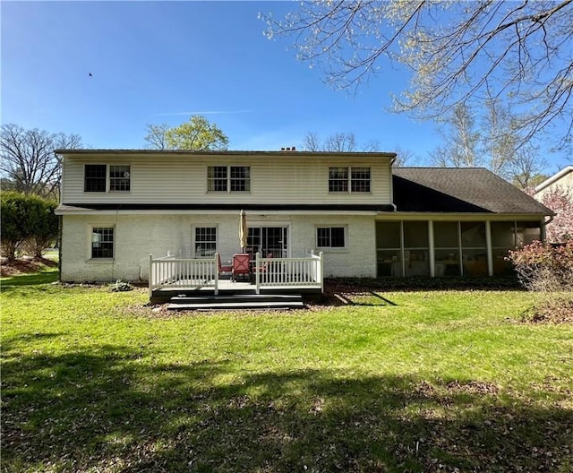 rear view of house with a lawn, brick siding, a sunroom, and a deck