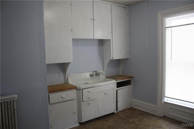 kitchen featuring baseboards, white cabinetry, radiator heating unit, and a wealth of natural light