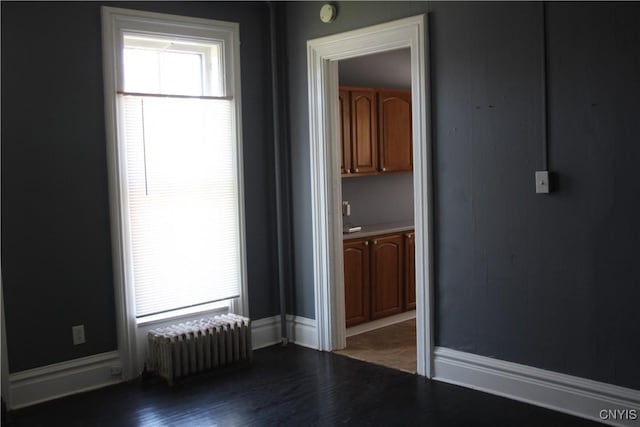 spare room with baseboards, radiator heating unit, and wood finished floors