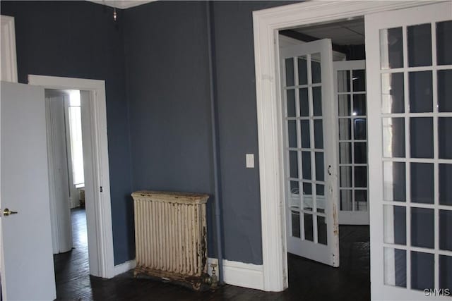empty room featuring baseboards, french doors, radiator heating unit, and wood finished floors
