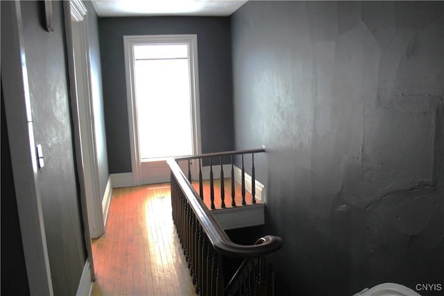 hall featuring baseboards, light wood-style flooring, and an upstairs landing