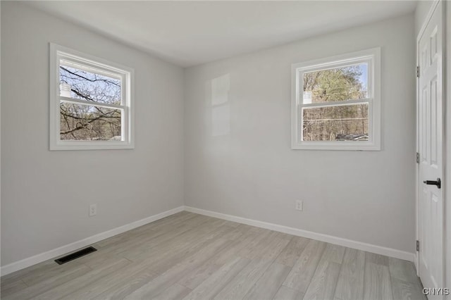 empty room featuring baseboards, a wealth of natural light, light wood finished floors, and visible vents