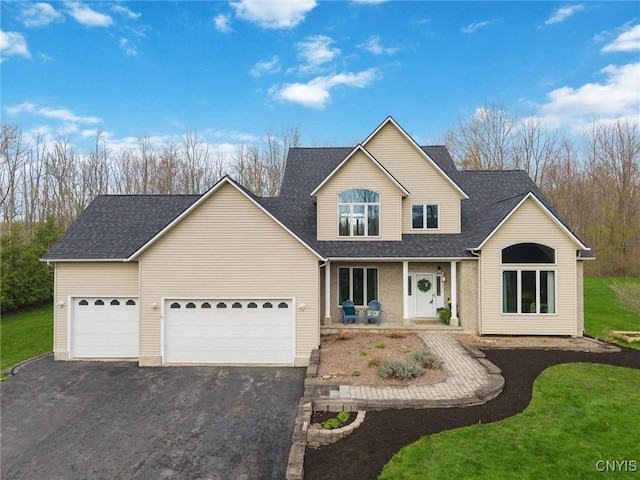 traditional home featuring a porch, driveway, a front yard, an attached garage, and a shingled roof