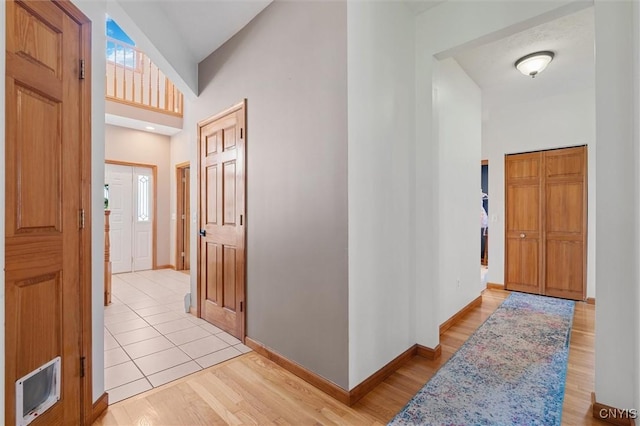 hallway with baseboards, a high ceiling, and light wood-style flooring