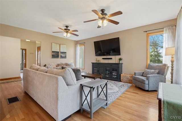 living room featuring a ceiling fan, baseboards, visible vents, and light wood-style flooring