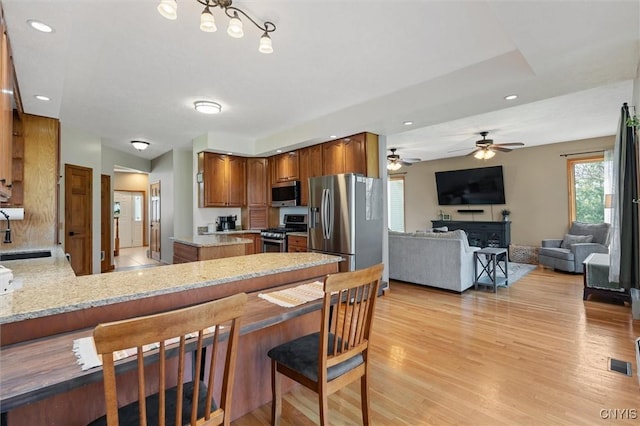 kitchen featuring brown cabinetry, light wood-type flooring, a sink, a peninsula, and stainless steel appliances