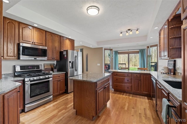 kitchen with light wood-style flooring, a raised ceiling, appliances with stainless steel finishes, and brown cabinets