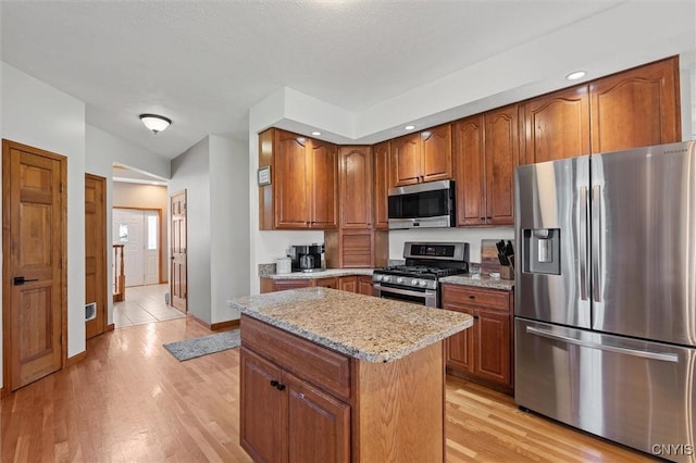 kitchen with brown cabinetry, a kitchen island, light stone countertops, stainless steel appliances, and light wood-style flooring