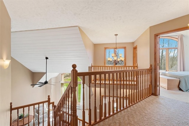 hallway with a chandelier, a textured ceiling, an upstairs landing, and carpet