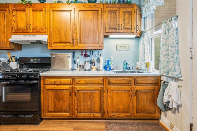 kitchen with brown cabinets, a sink, light countertops, black gas stove, and under cabinet range hood